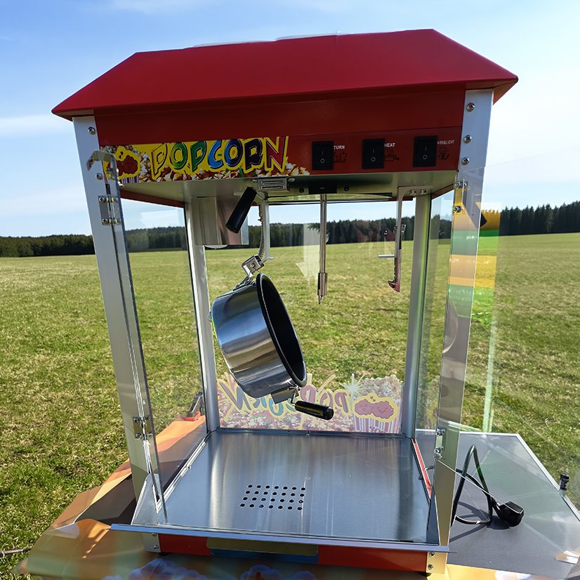 Eine Popcornmaschine um Popcorn selbst herzustellen. Sie hat einen metallischen Rahmen und eine rote Abdecung mit großer Aufschrift.